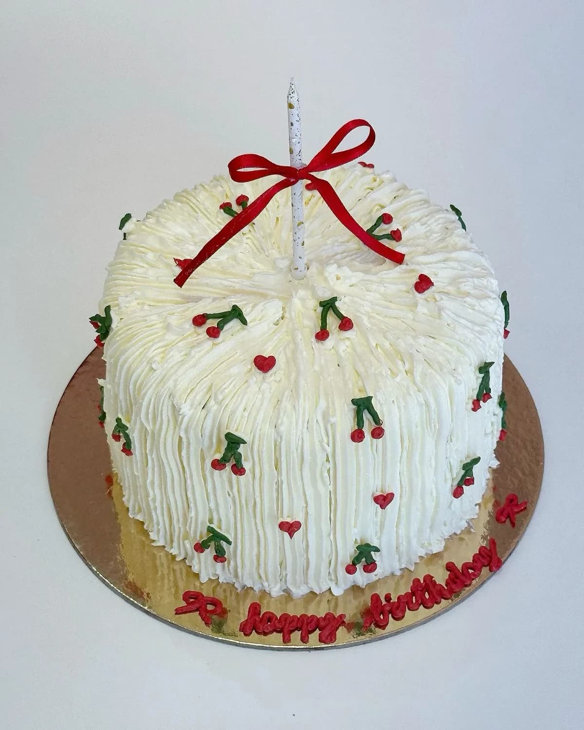 White buttercream birthday cake piped in vintage style with cherries, hearts and a ribbon-tied candle, a custom cake by Cakes By Vjollca in Pristina, Kosovo