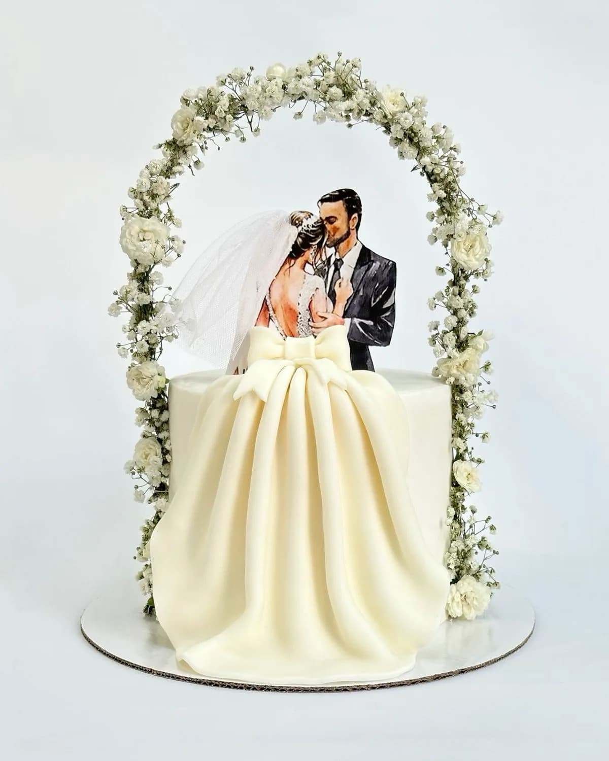 Engagement cake with a couple topper under a white floral arch and a draped fondant gown, a custom cake by Cakes By Vjollca in Pristina, Kosovo