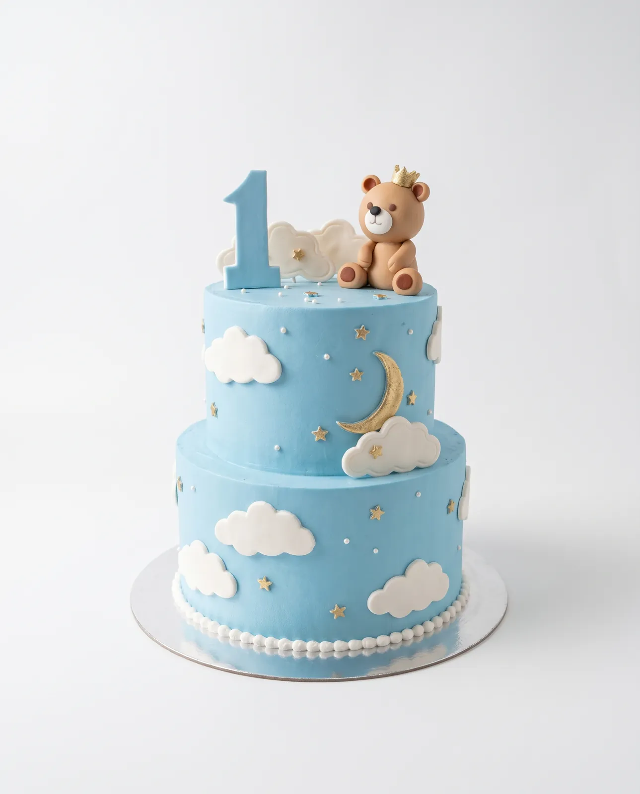 Torte blu qielli me dy kate për ditëlindjen e parë me arush prej fondani me kurorë, numrin 1 në blu, re të bardha, hënë gjysmë ari dhe yje ari, torte me porosi nga Cakes By Vjollca në Prishtinë
