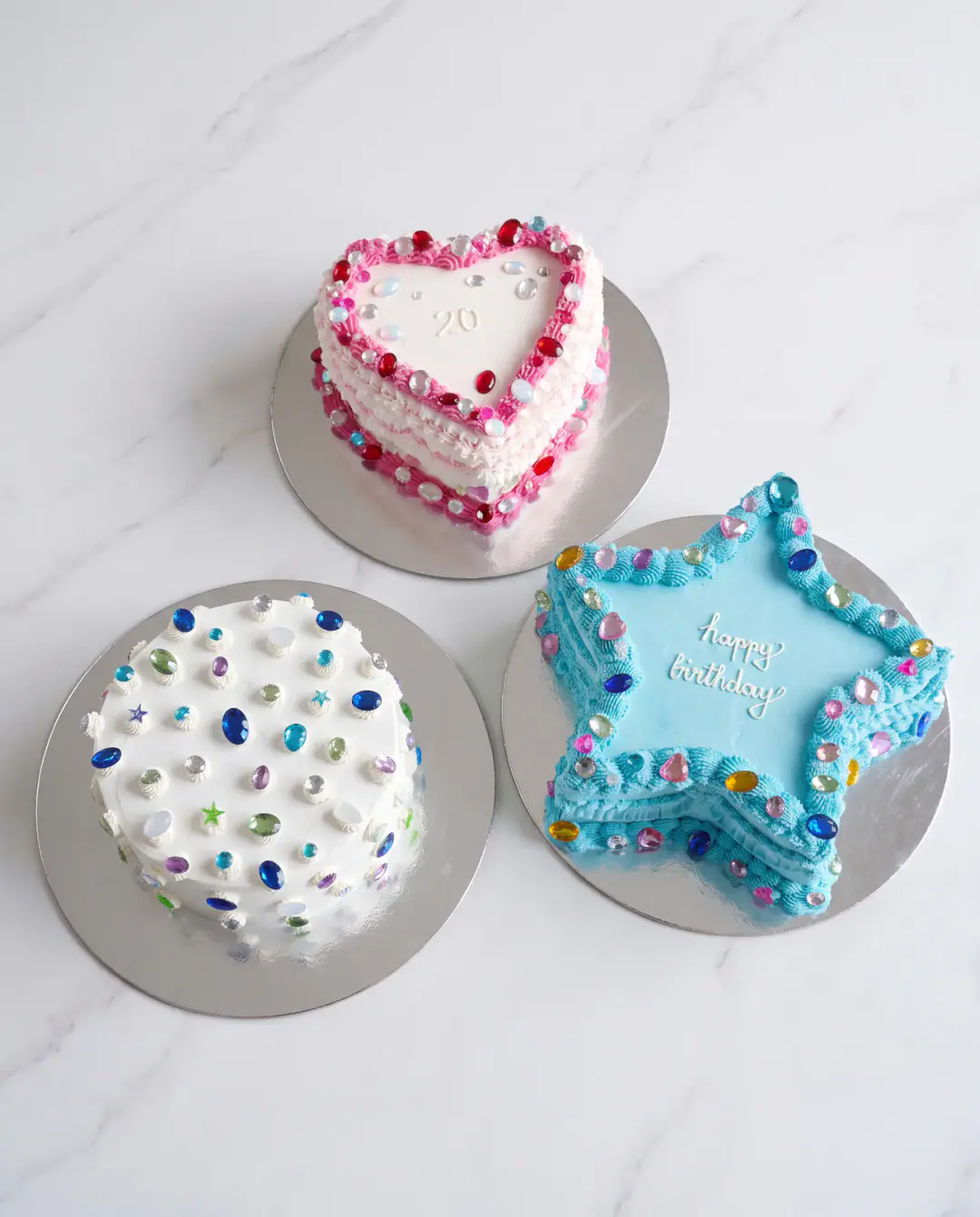 Tre torta të vogla ditëlindjeje në stil vintage me xhevahire sheqeri: një zemër rozë, një e rrumbullakët e bardhë dhe një yll blu, torta me porosi nga Cakes By Vjollca në Prishtinë