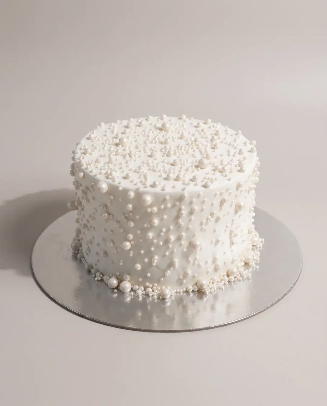 Tall white cake covered in scattered sugar pearls of different sizes, with larger pearls gathered at the base, a custom cake by Cakes By Vjollca in Pristina, Kosovo