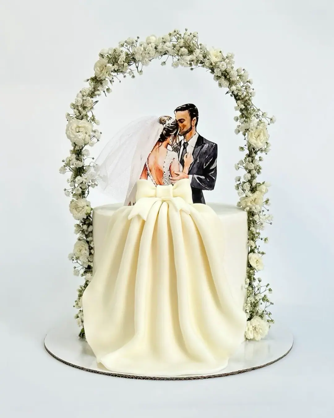 Engagement cake with a couple topper under a white floral arch and a draped fondant gown, a custom cake by Cakes By Vjollca in Pristina, Kosovo