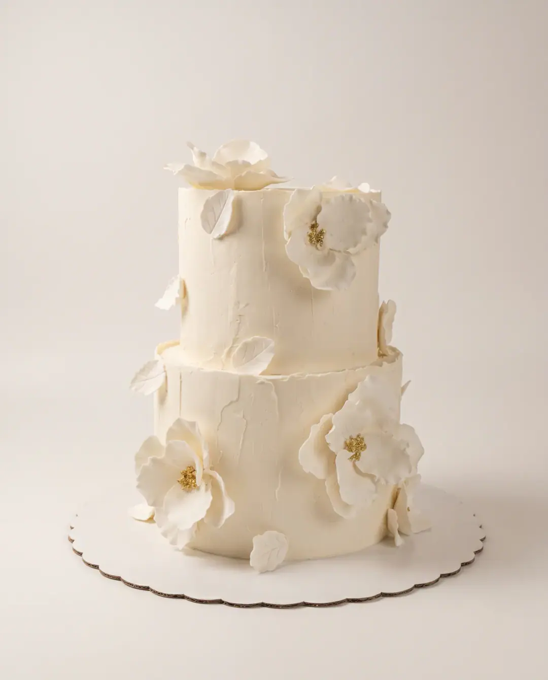 Two-tier textured ivory engagement cake with open white sugar flowers, gold-dusted centres and white sugar leaves, a custom cake by Cakes By Vjollca in Pristina, Kosovo