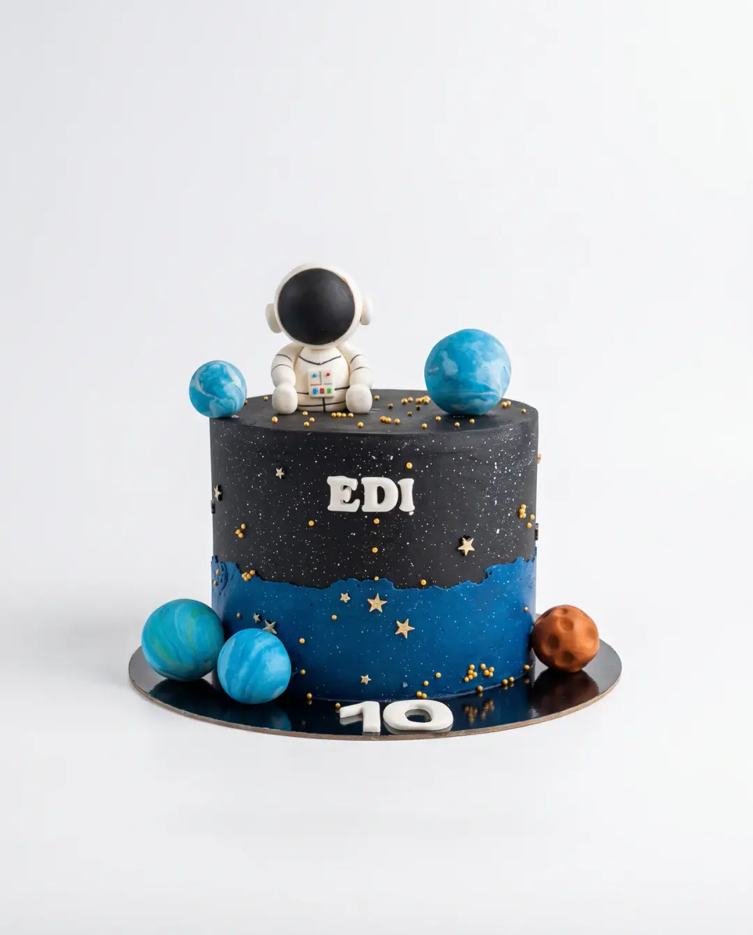 Black and blue galaxy birthday cake with a fondant astronaut, marbled planets, gold stars, the child's name and the number 10, a custom cake by Cakes By Vjollca in Pristina, Kosovo
