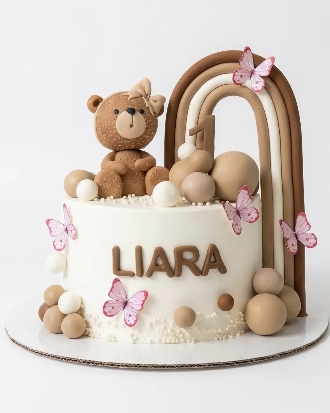Neutral boho first birthday cake with a teddy bear, rainbow arch and butterflies, a custom cake by Cakes By Vjollca in Pristina, Kosovo