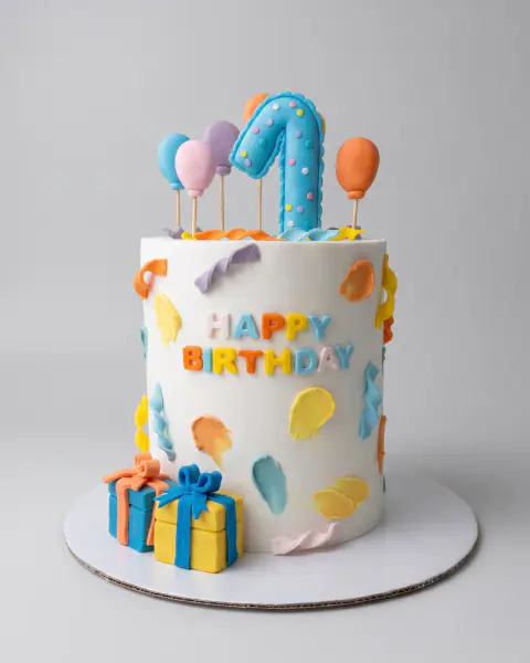 Tall white first birthday cake with fondant balloons, gift boxes and a number one topper, a custom cake by Cakes By Vjollca in Pristina, Kosovo
