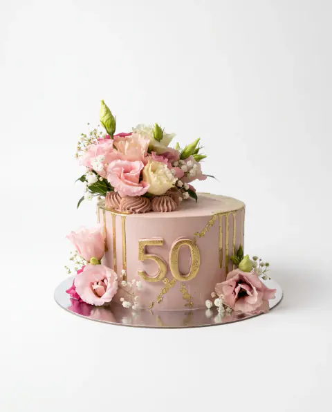 Blush pink 50th birthday cake with gold drips and a gold number, topped with fresh lisianthus, cream roses, baby's breath and pink meringue kisses, a custom cake by Cakes By Vjollca in Pristina, Kosovo