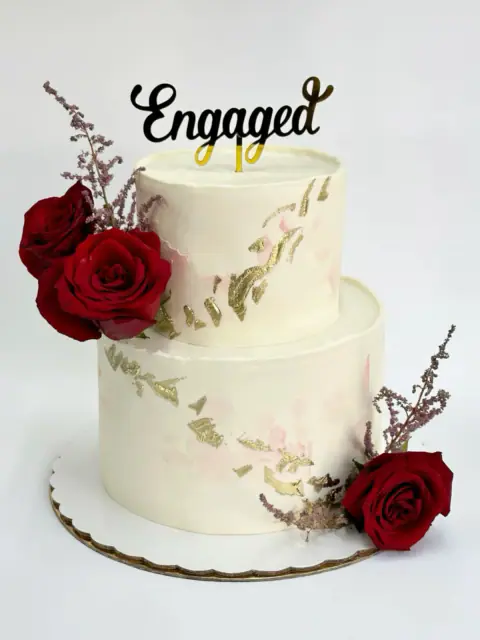 Two-tier engagement cake with fresh red roses and a gold Engaged topper, a custom cake by Cakes By Vjollca in Pristina, Kosovo