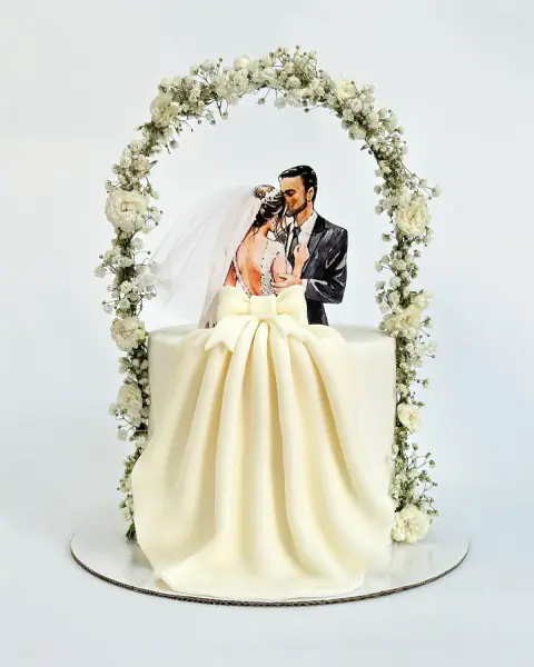 Engagement cake with a couple topper under a white floral arch and a draped fondant gown, a custom cake by Cakes By Vjollca in Pristina, Kosovo