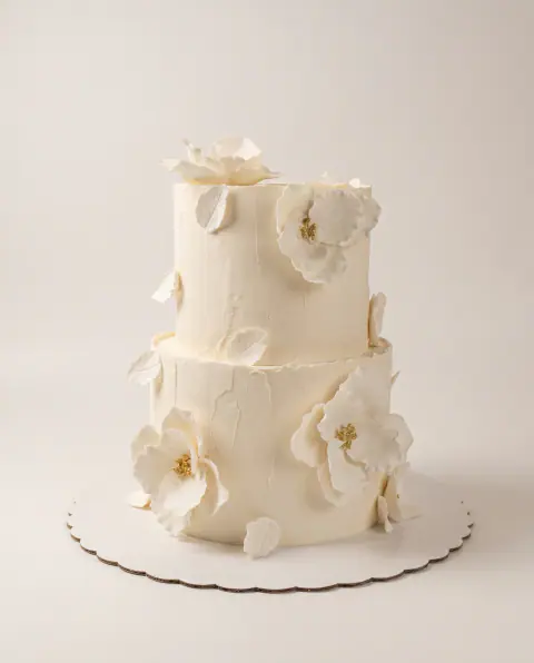 Torte fejese me dy kate në fildish me teksturë, lule sheqeri të bardha të hapura me qendra të praruara dhe gjethe sheqeri të bardha, torte me porosi nga Cakes By Vjollca në Prishtinë