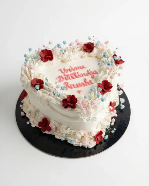 White heart cake with red and pink sugar blossoms and a piped birthday wish, a custom cake by Cakes By Vjollca in Pristina, Kosovo