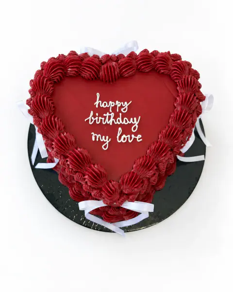 Deep red vintage heart cake with ruffled red piping, white satin bows and 'happy birthday my love' written in white script, a custom cake by Cakes By Vjollca in Pristina, Kosovo