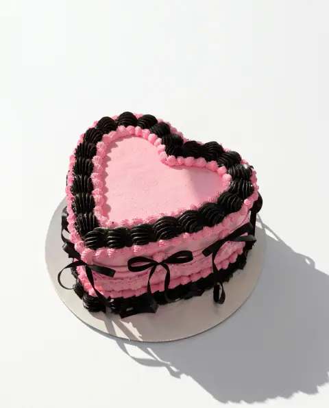 Pink vintage heart cake with black piped shell borders, ruffled pink sides and black satin ribbons tied into bows, a custom cake by Cakes By Vjollca in Pristina, Kosovo