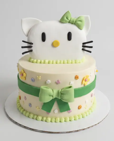 Two-tier Hello Kitty cake with green bows and sugar flowers, a custom cake by Cakes By Vjollca in Pristina, Kosovo
