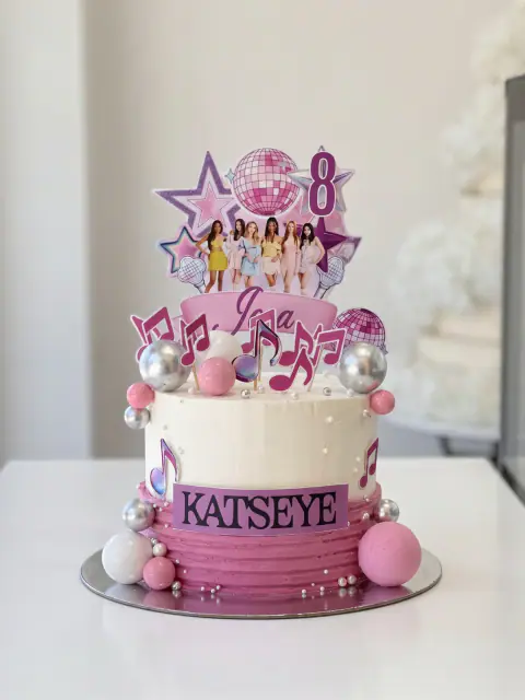Torte ditëlindjeje KATSEYE në të bardhë e rozë me dekor të printuar të grupit, topa disko, yje, nota muzikore, topa argjendi e rozë dhe numrin 8, torte me porosi nga Cakes By Vjollca në Prishtinë