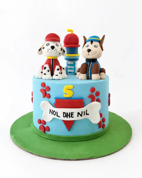 Sky-blue Paw Patrol birthday cake with modelled fondant Marshall and Chase, the lookout tower, red paw prints, a bone name plaque and the number 5 on a green grass board, a custom cake by Cakes By Vjollca in Pristina, Kosovo